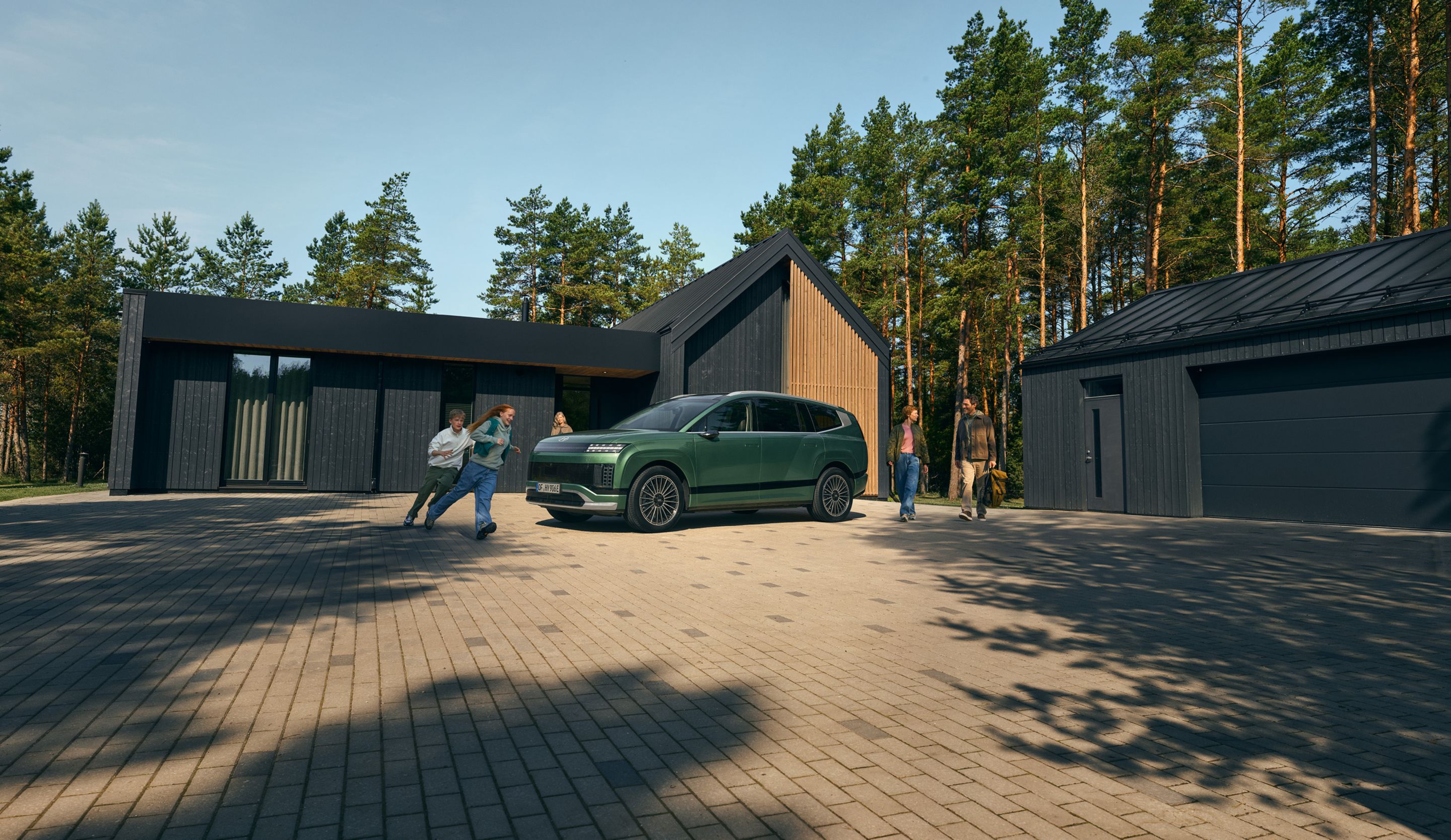 Vista lateral del Hyundai IONIQ 9, SUV eléctrico, con niños corriendo alrededor frente a una casa. 